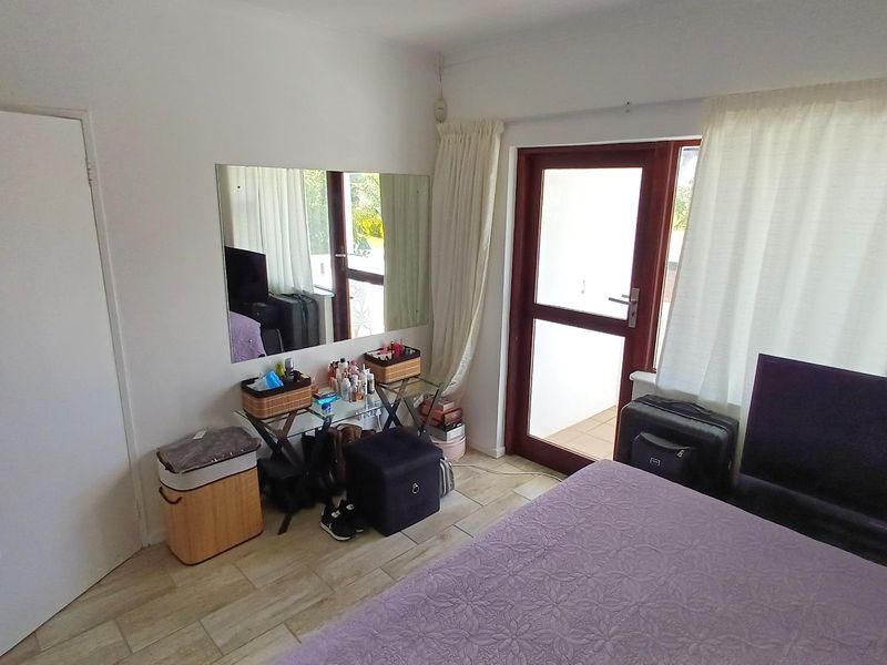 A bedroom featuring tiled flooring and a glass door providing access to an outdoor area, with a wall-mounted mirror.