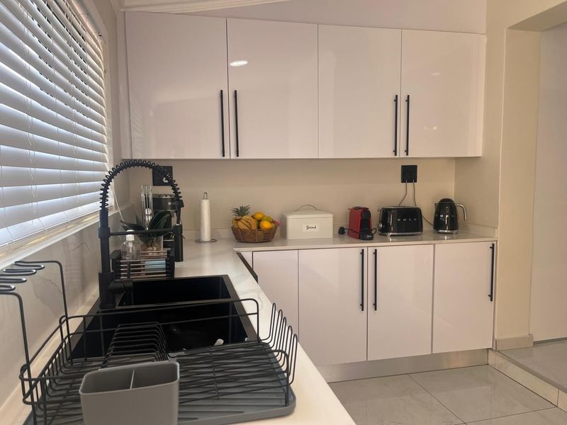 A modern kitchen featuring white gloss cabinetry, a black matte faucet with a matching undermount sink, and stone-look countertops.