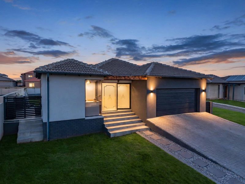 Modern single-story residential home featuring a tiled roof, double garage, paved driveway, and well-maintained front garden at dusk.