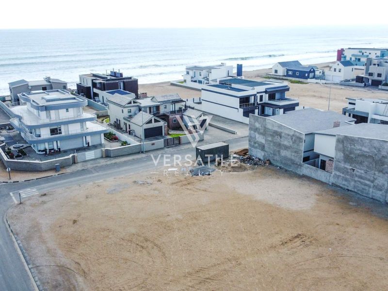 An aerial view of a vacant residential plot situated in a coastal neighborhood with established surrounding properties and street access.