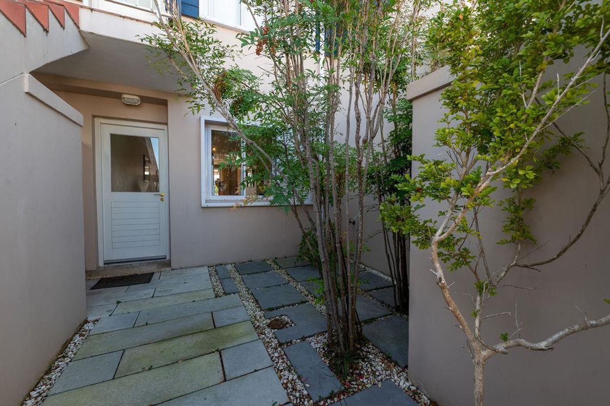 A private courtyard entrance featuring stone paving, established trees, and a secure exterior door leading into the apartment.
