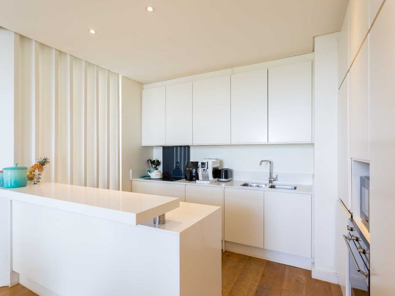 Modern kitchen featuring sleek white cabinetry, stone countertops, a breakfast bar, integrated appliances, and warm hardwood flooring.