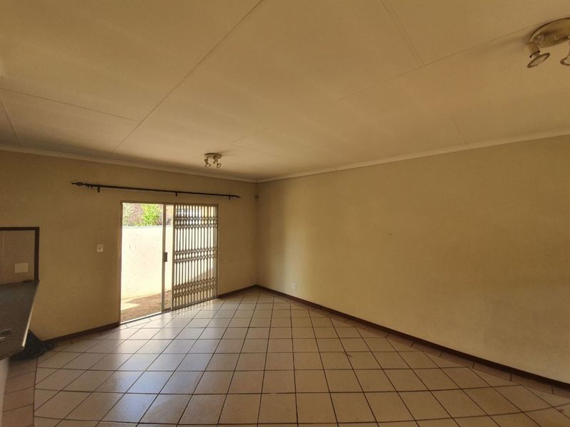 An empty living room featuring ceramic floor tiles, a sliding glass door with a security gate, and neutral wall finishes.