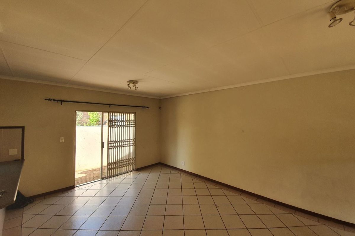 An empty living room featuring ceramic floor tiles, a sliding glass door with a security gate, and neutral wall finishes.