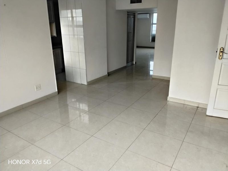 An empty open-plan living area featuring neutral tiled flooring, clean white walls, and an integrated air conditioning unit.