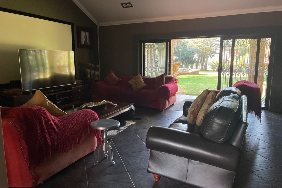 Spacious living room featuring dark tiled flooring, vaulted ceilings with recessed lighting, and large sliding glass doors providing direct access to the garden.