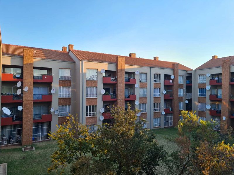 Exterior view of a multi-story apartment complex featuring brick accents, private balconies, and a shared communal garden area.