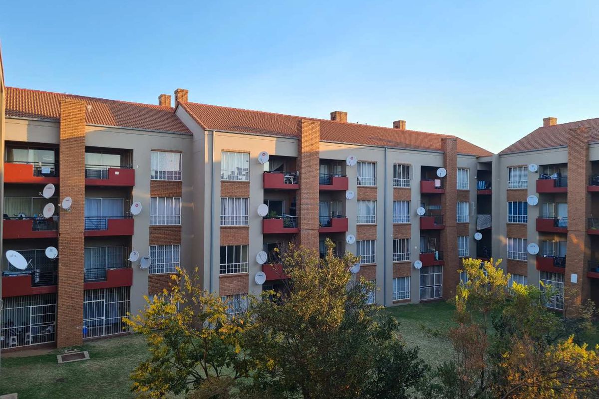 Exterior view of a multi-story apartment complex featuring brick accents, private balconies, and a shared communal garden area.