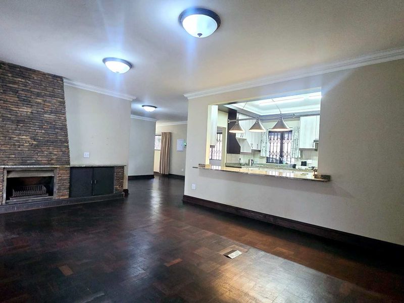 Spacious open-plan living area featuring a stone-clad fireplace, built-in shelving, and a breakfast bar connecting to the kitchen, finished with classic parquet flooring.