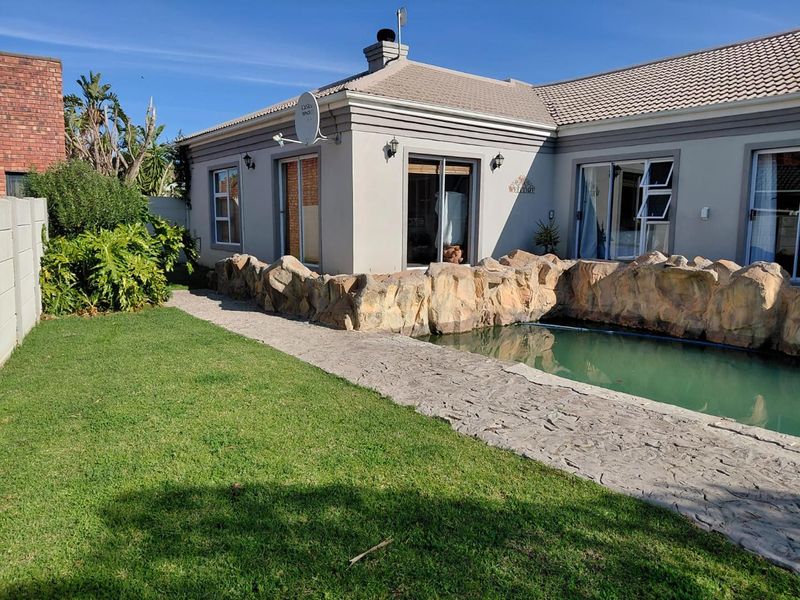 Rear exterior view featuring a swimming pool with a decorative rock surround, paved walkway, and direct access to the home via sliding glass doors.