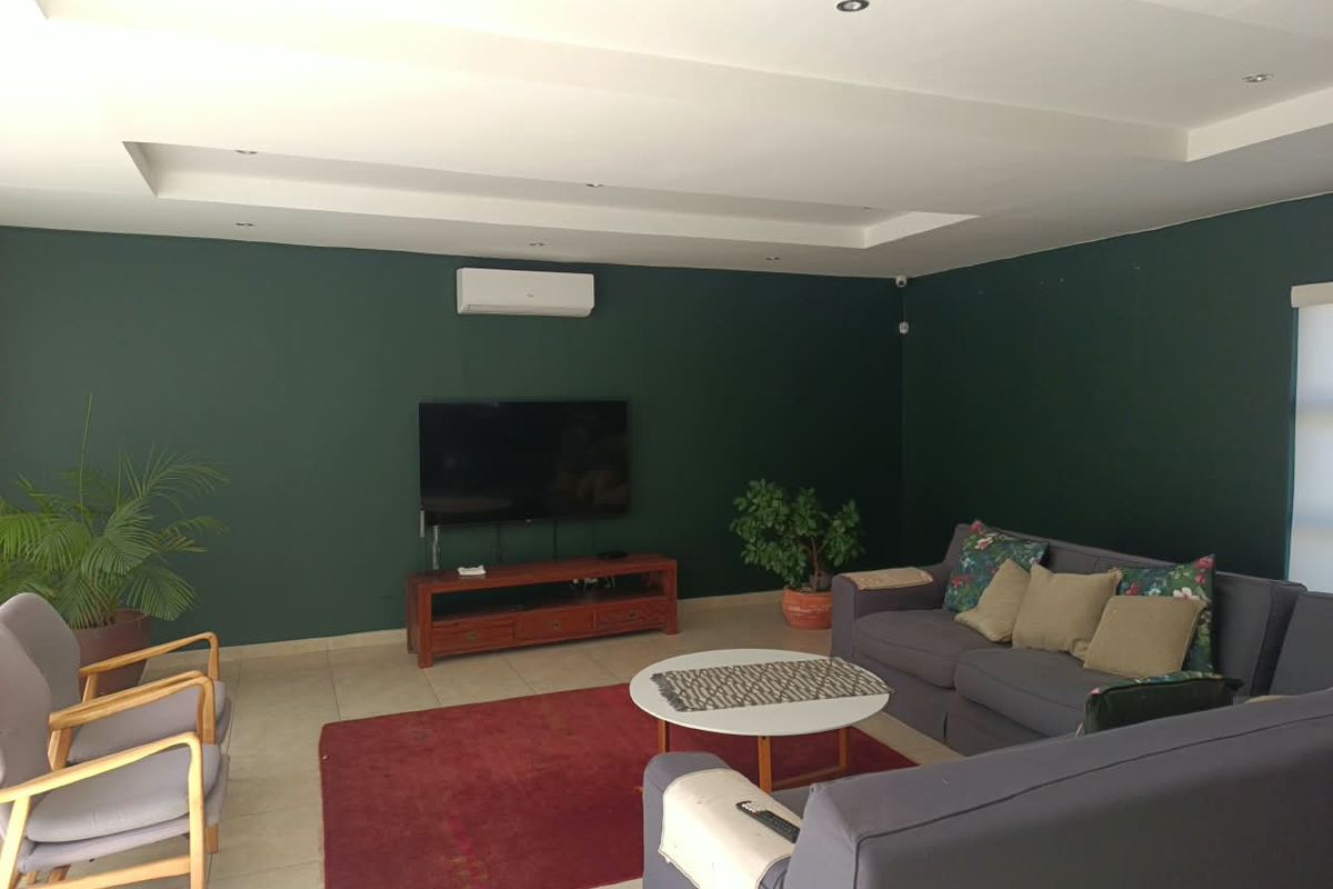 A spacious living room featuring a recessed ceiling with downlights, tiled flooring, and a wall-mounted split-system air conditioner.
