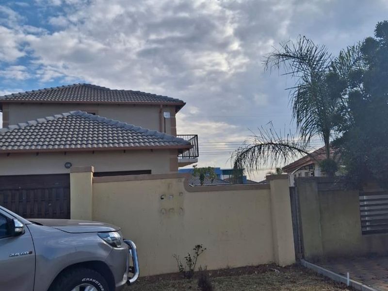 Front exterior view of a two-story residential property featuring a tiled roof, perimeter wall, and paved driveway area.