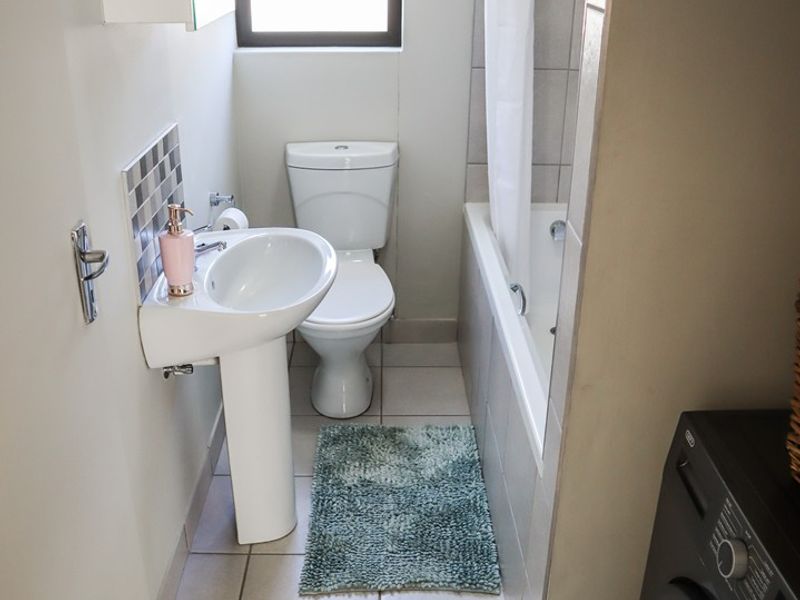 Compact bathroom featuring a pedestal basin, toilet, and a bathtub with shower facilities, finished with neutral floor and wall tiling.