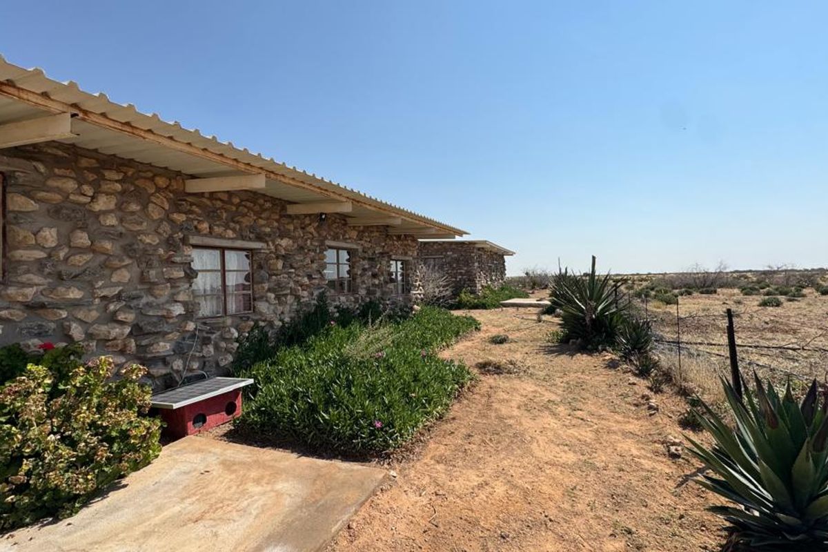 Rear view of a rustic stone farmhouse featuring a corrugated metal roof, metal-framed windows, and a surrounding natural landscape.