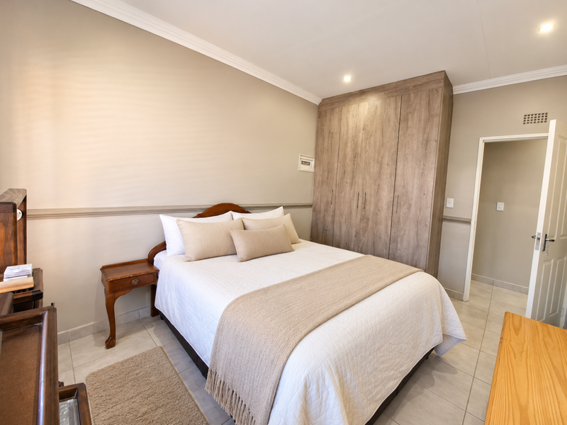 A well-maintained bedroom featuring neutral walls, tiled flooring, crown molding, and ample built-in cupboard storage.