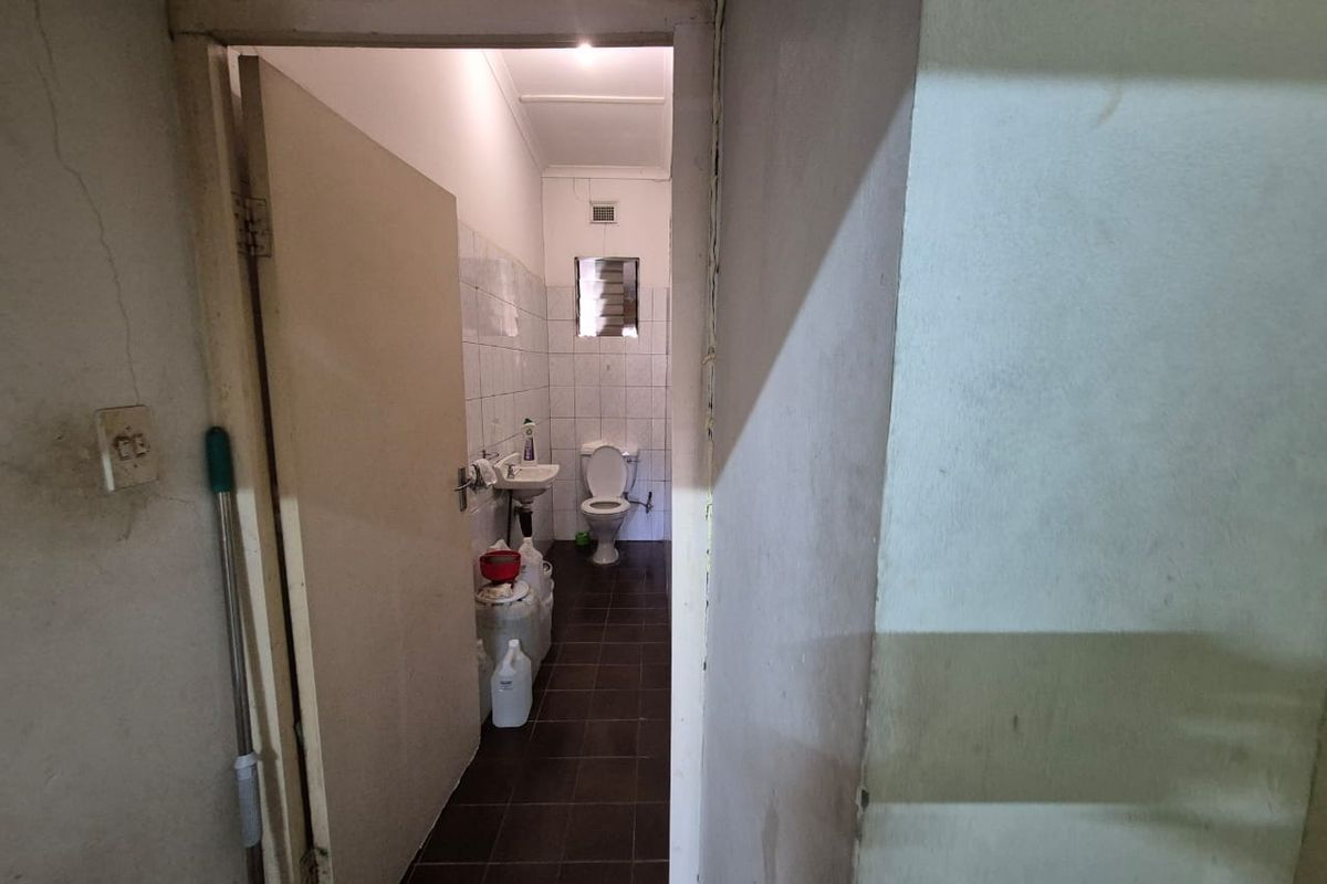 A small, dated bathroom featuring a wall-mounted basin and toilet, with tiled finishes requiring maintenance and cosmetic updates.