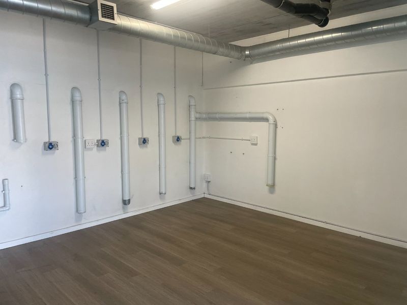 An empty utility space featuring exposed industrial ductwork, visible piping, multiple electrical outlets, and modern laminate flooring.