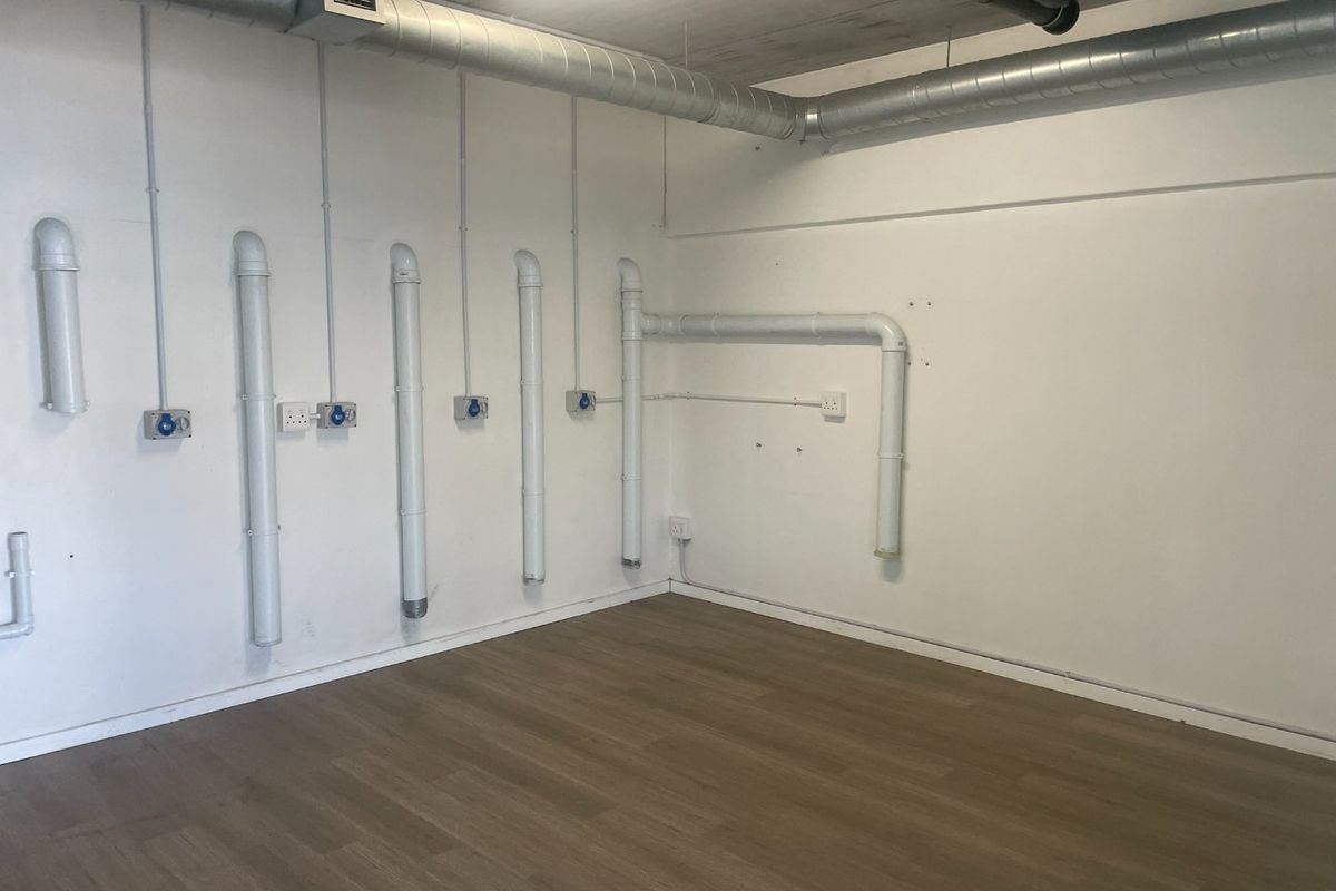 An empty utility space featuring exposed industrial ductwork, visible piping, multiple electrical outlets, and modern laminate flooring.