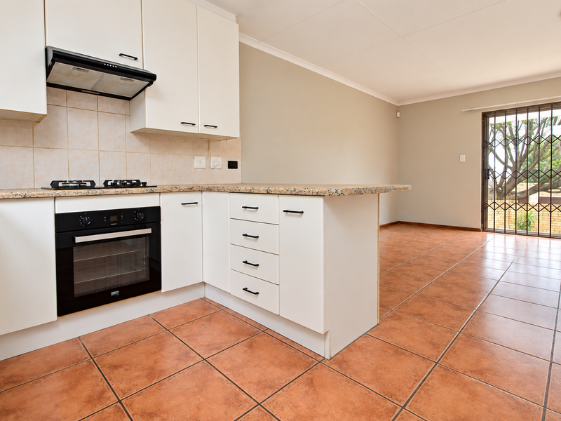 Open-plan kitchen and living area featuring tiled flooring, white cabinetry, granite countertops, and direct access to the exterior through a security gate.