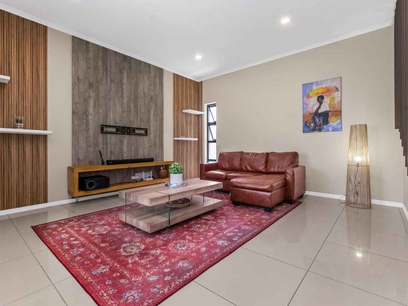 A modern living room featuring tiled flooring, recessed downlighting, and a decorative feature wall with integrated floating shelving.