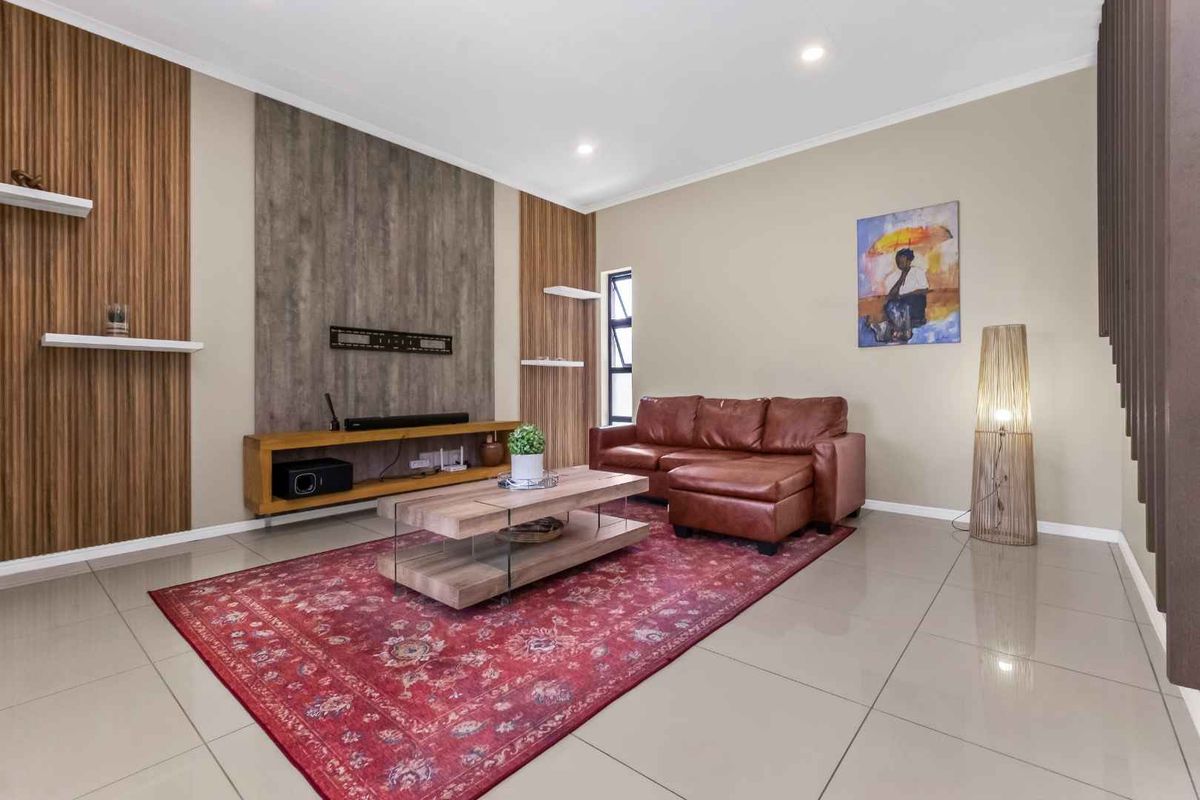 A modern living room featuring tiled flooring, recessed downlighting, and a decorative feature wall with integrated floating shelving.