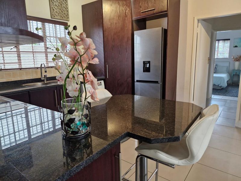Modern kitchen featuring dark wood cabinetry, granite countertops, a breakfast bar, and tiled flooring, with a view into the adjacent bedroom.