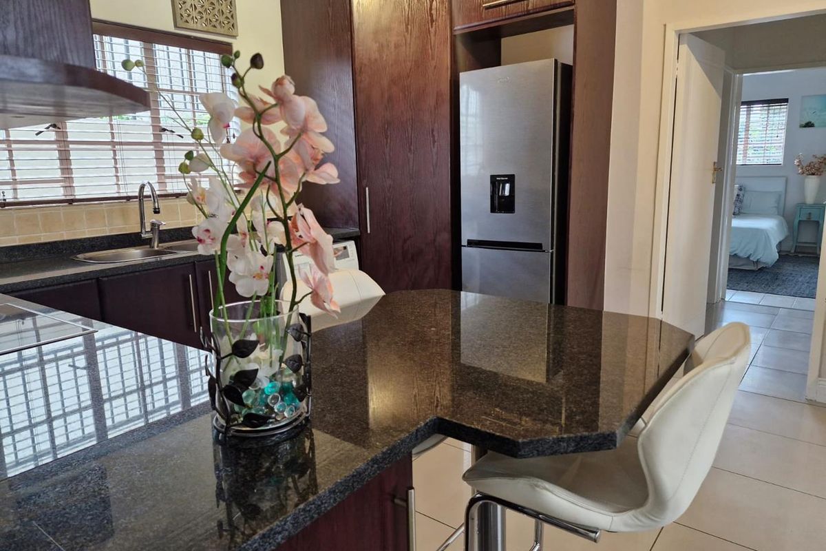 Modern kitchen featuring dark wood cabinetry, granite countertops, a breakfast bar, and tiled flooring, with a view into the adjacent bedroom.