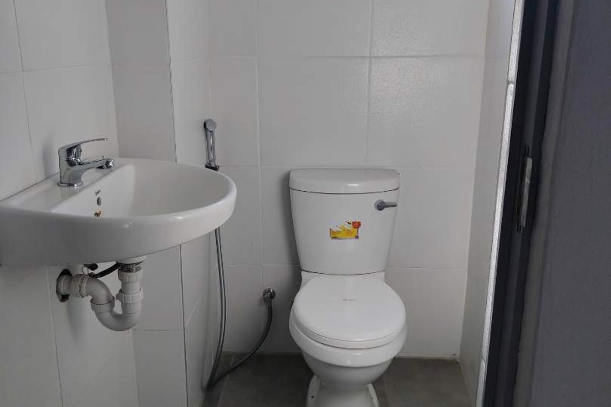 A compact office restroom featuring white wall tiles, a pedestal sink, a standard toilet, and a small window for ventilation.