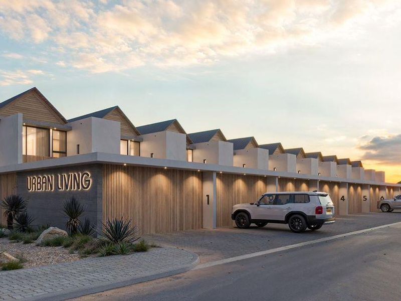 A modern townhouse complex exterior featuring a row of garages, contemporary architectural design, and paved driveway access at sunset.