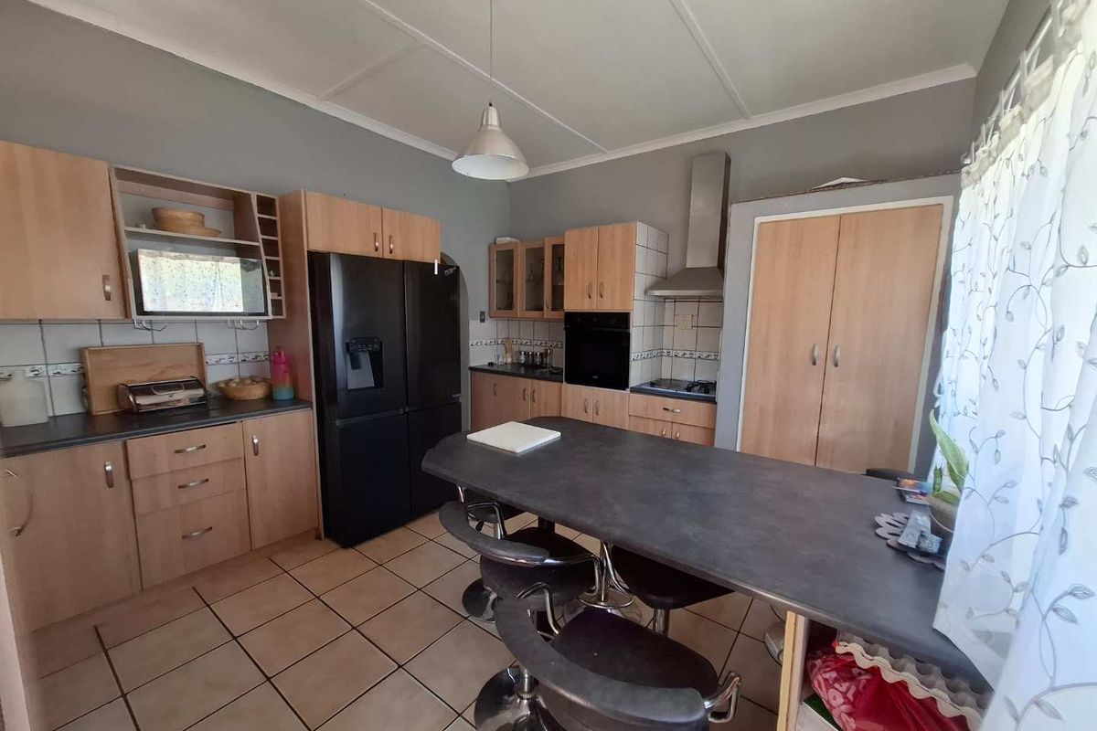 Functional kitchen featuring light wood-tone cabinetry, dark countertops, built-in oven, extractor fan, and a central breakfast bar island with tiled flooring.