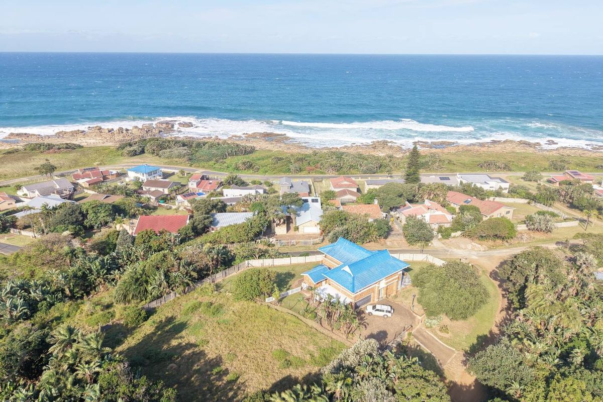 Aerial view of a coastal residential property featuring a detached home with a blue roof, situated in a scenic seaside neighborhood.