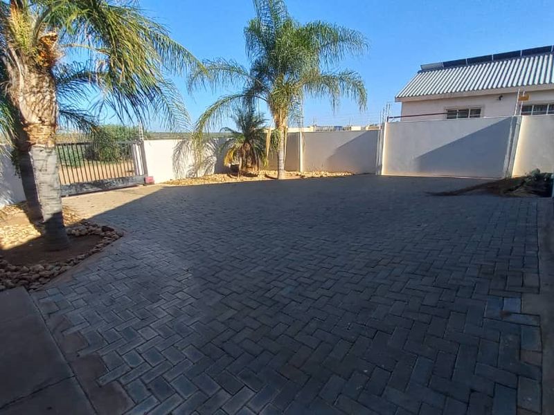 A spacious paved driveway area featuring perimeter walls with electric fencing, a sliding gate, and established palm trees.