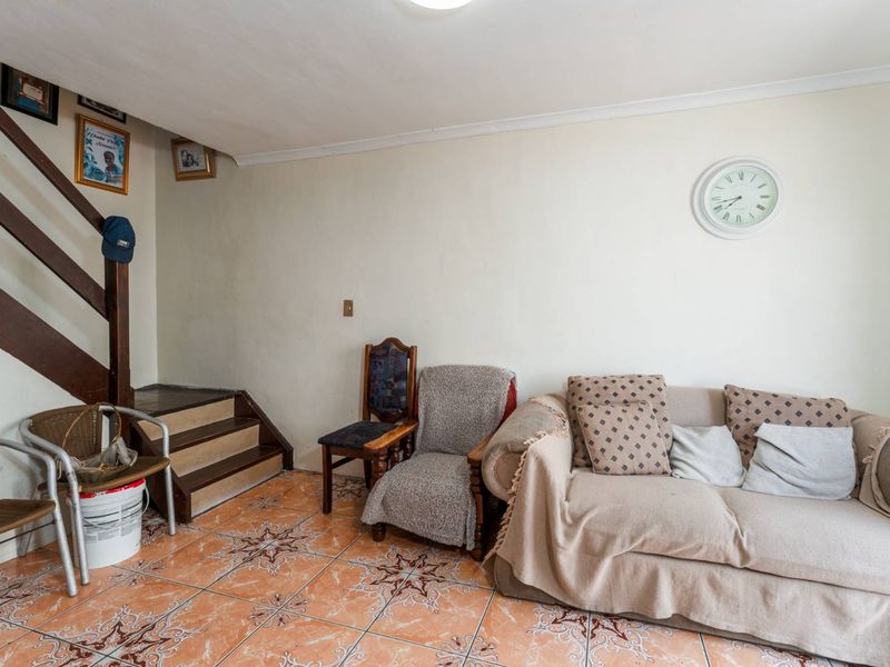 Living area featuring ceramic floor tiles and a wooden staircase, offering a functional space with potential for cosmetic updates.