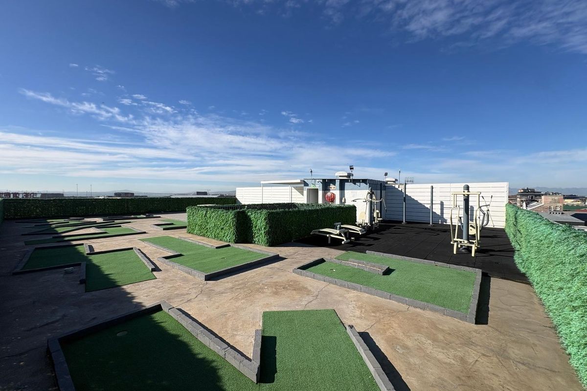 Rooftop recreational area featuring a miniature golf course and outdoor fitness equipment, enclosed by perimeter hedging and fencing.