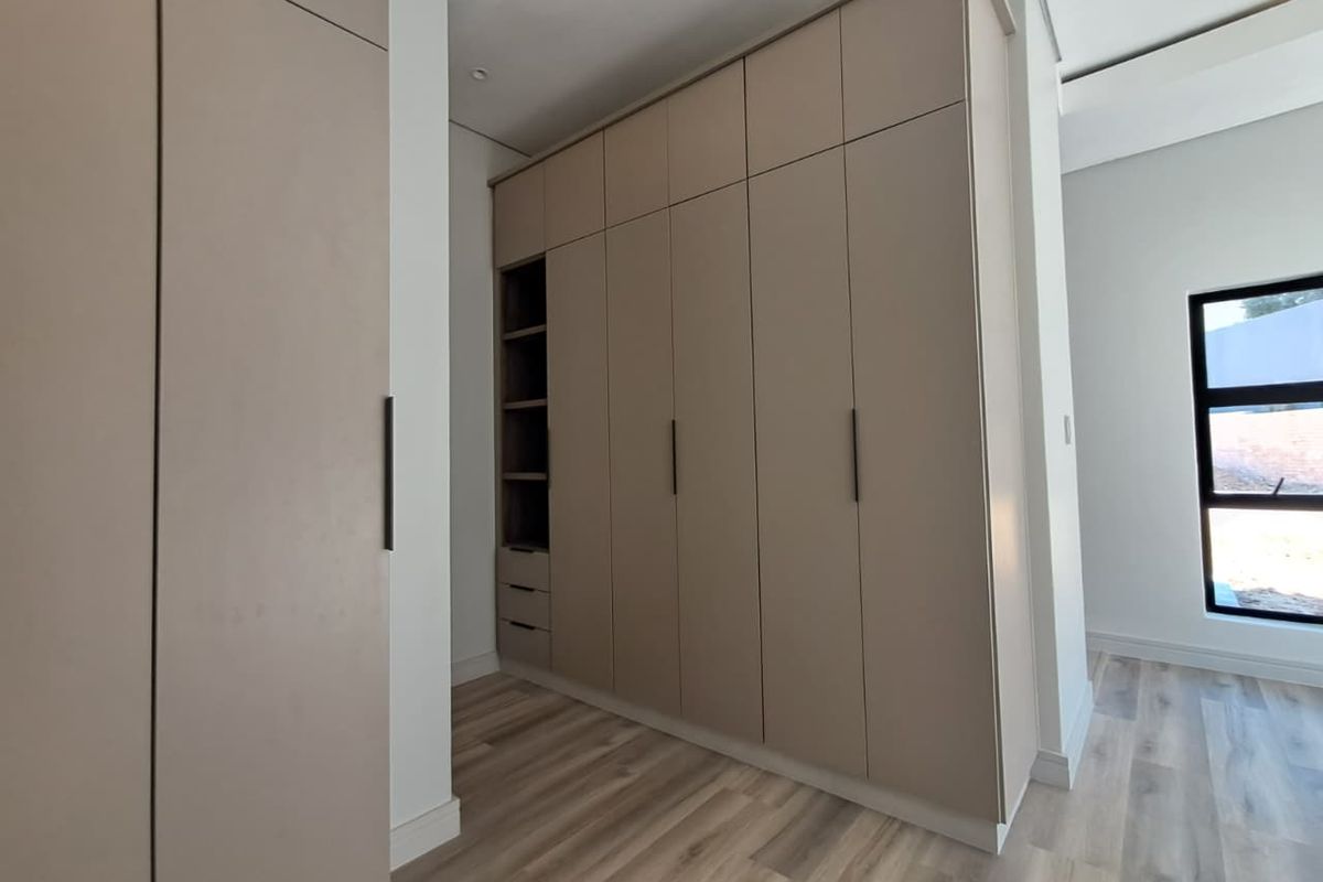 A modern bedroom featuring extensive floor-to-ceiling built-in cupboards, light wood-look laminate flooring, and clean, contemporary finishes.