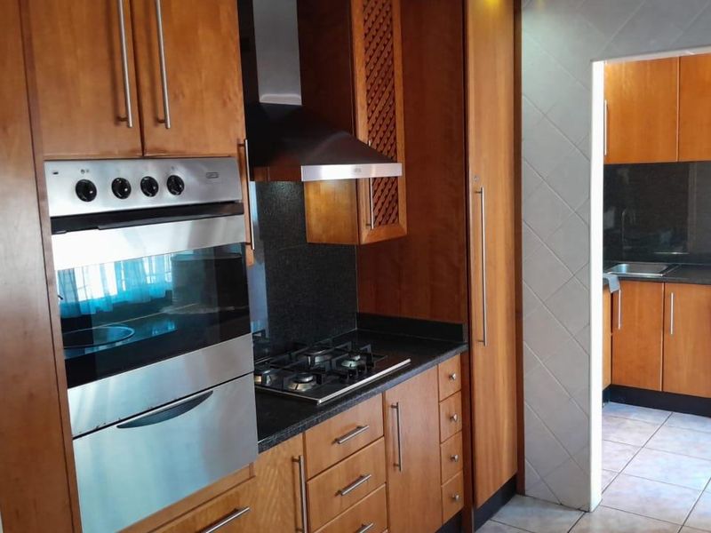 A functional kitchen featuring wooden cabinetry, granite countertops, a built-in oven, and a gas hob, with an adjacent scullery area visible through the doorway.