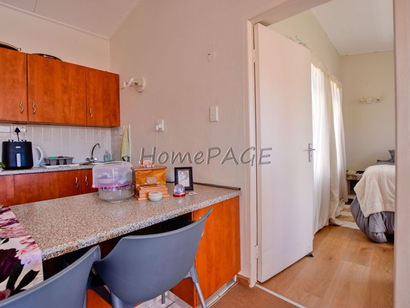 Compact kitchen area featuring laminate cabinetry, granite-look countertops, and a tiled splashback, with direct access to the adjacent bedroom.