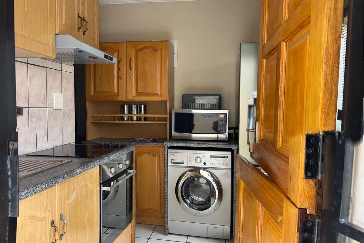 Compact kitchen featuring wooden cabinetry, granite-look countertops, built-in oven, hob, extractor fan, and integrated laundry appliance space.