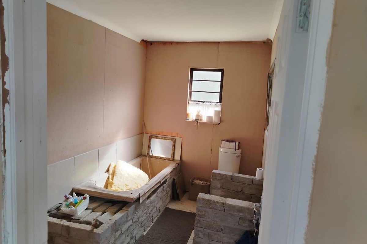A bathroom in the process of renovation, featuring exposed brickwork, unfinished walls, and a partially installed bathtub and toilet.