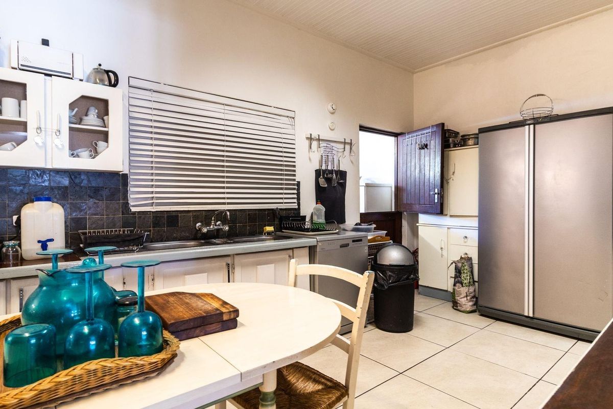 A functional kitchen featuring tiled flooring, dark backsplash tiling, white cabinetry, and a double sink, with direct access to an exterior door.