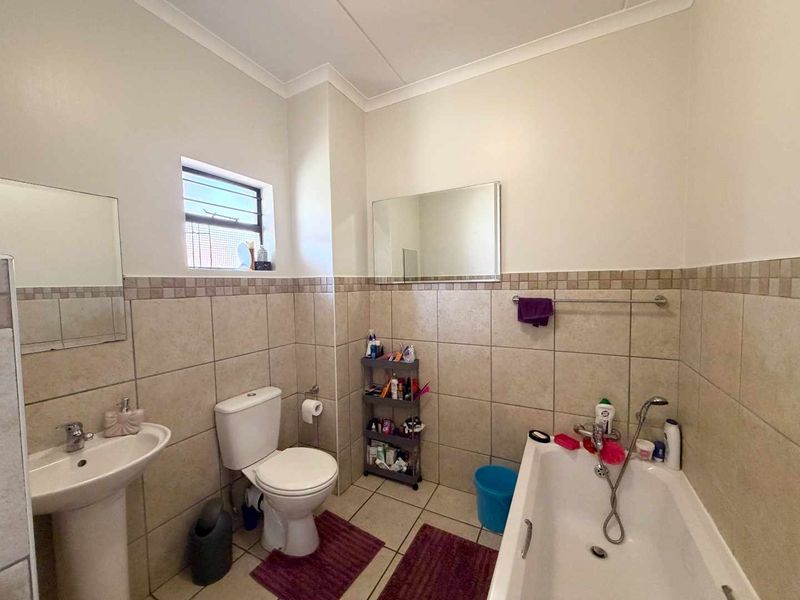 A functional bathroom featuring a pedestal basin, toilet, and bathtub with neutral wall tiling and a window for natural light.