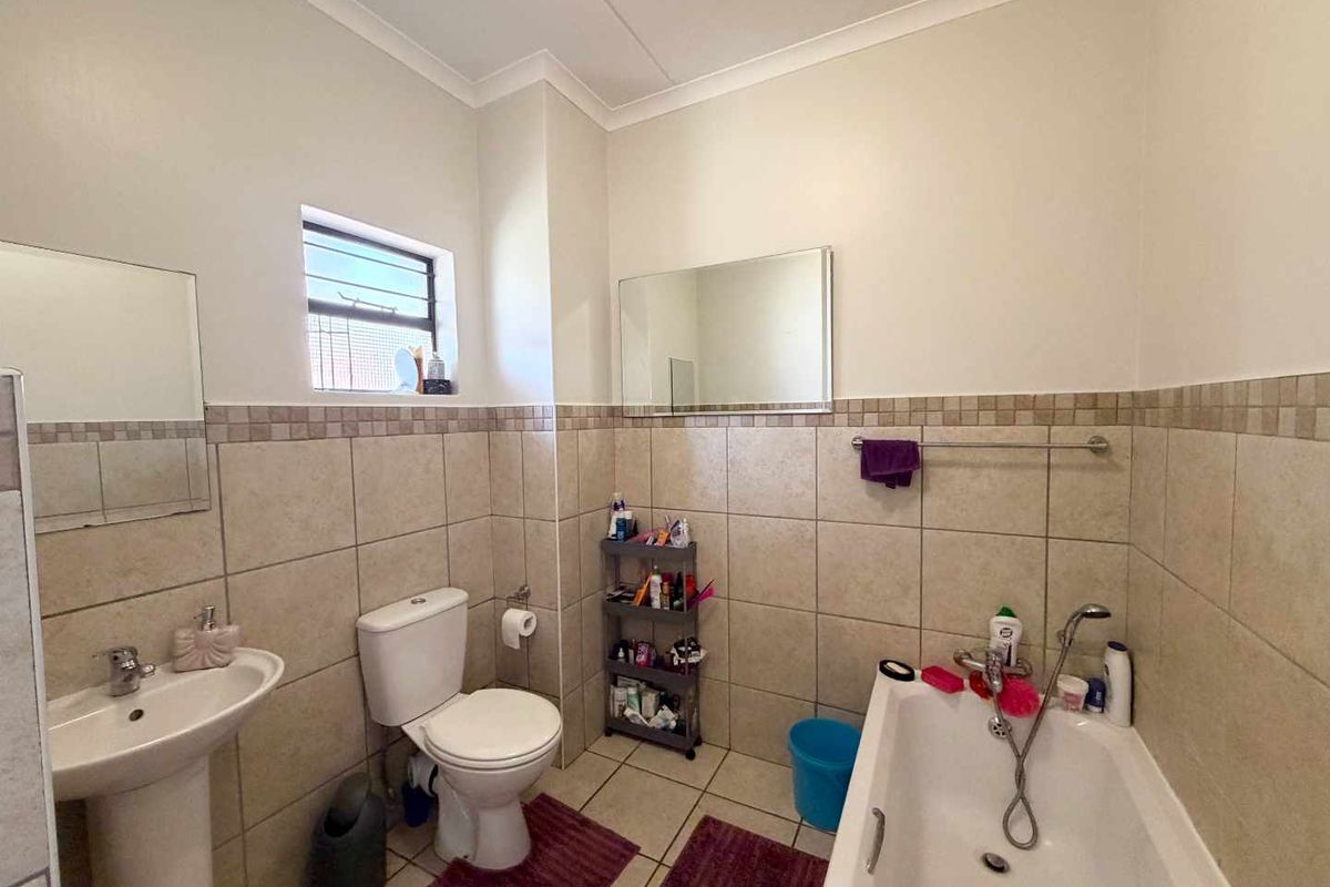 A functional bathroom featuring a pedestal basin, toilet, and bathtub with neutral wall tiling and a window for natural light.
