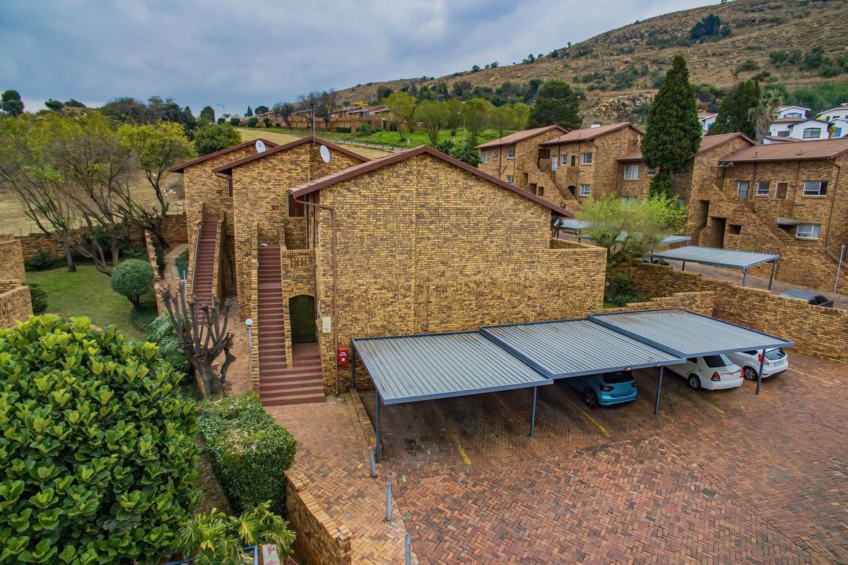 Aerial view of a townhouse complex featuring face-brick architecture, covered carports, and paved driveway areas set within a landscaped estate.