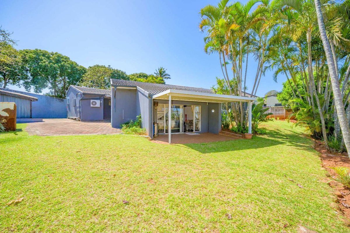 Rear view of the house featuring a covered patio, paved driveway, and a spacious garden with mature palm trees.