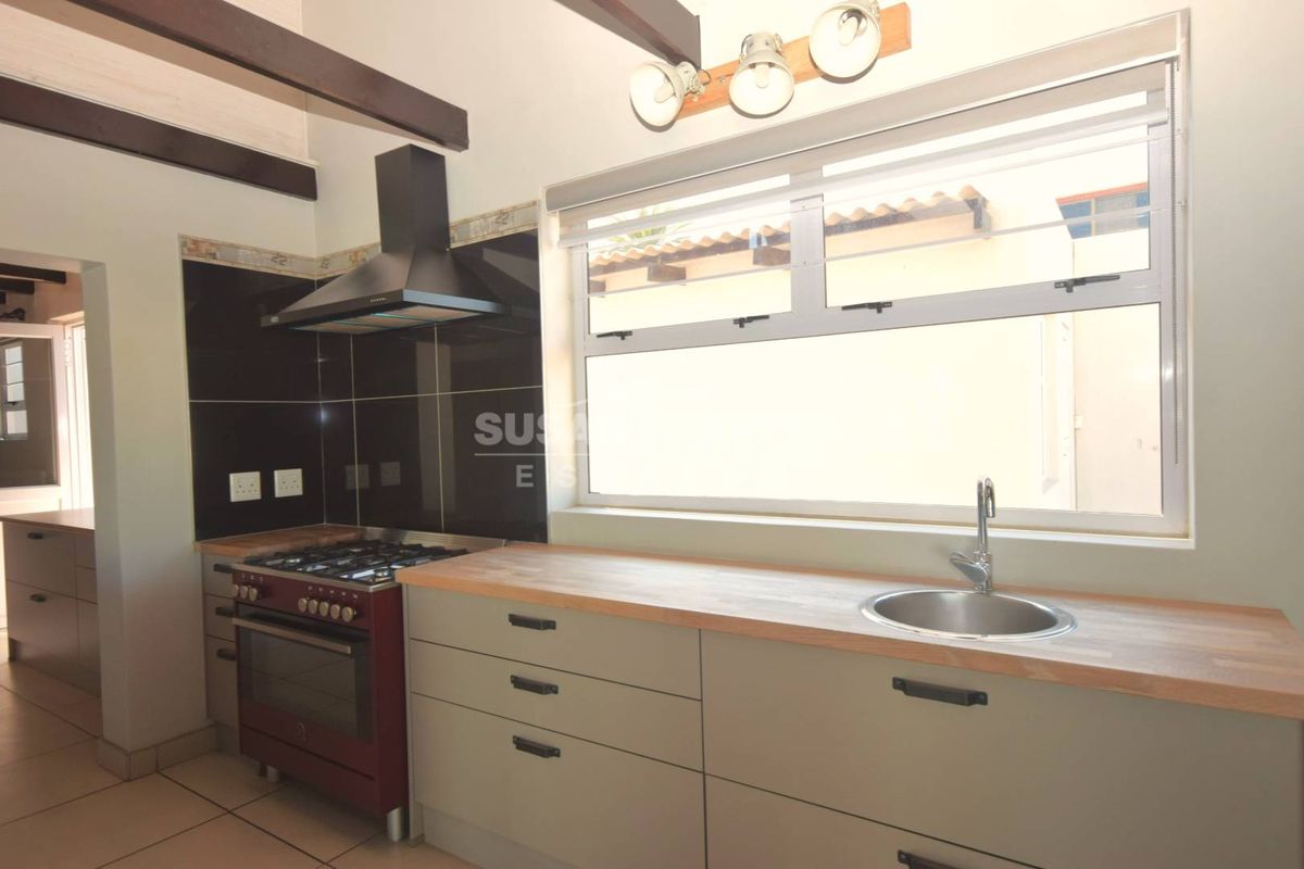 Modern kitchen featuring wooden countertops, stainless steel sink, gas stove with extractor fan, and exposed ceiling beams, offering a clean and functional workspace.