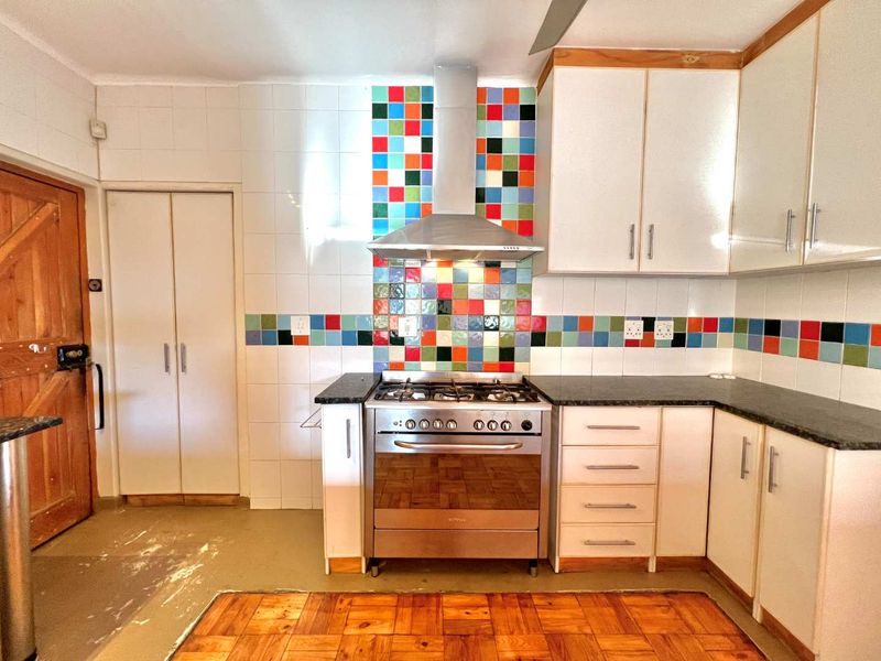 A functional kitchen featuring a gas stove, stainless steel extractor fan, granite countertops, and a distinctive multi-colored tiled splashback with ample built-in cabinetry.