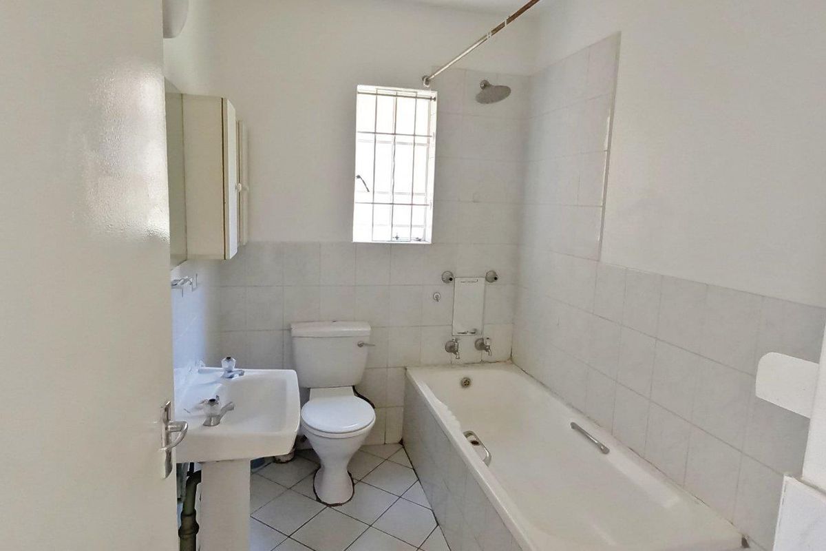 A functional bathroom featuring a pedestal basin, toilet, and a bathtub with a shower head, finished with white wall tiles and tiled flooring.
