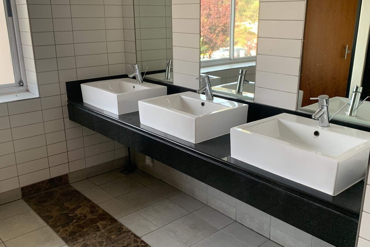 A modern office restroom featuring a triple vanity with white vessel sinks, black granite countertop, and large wall-mounted mirrors.