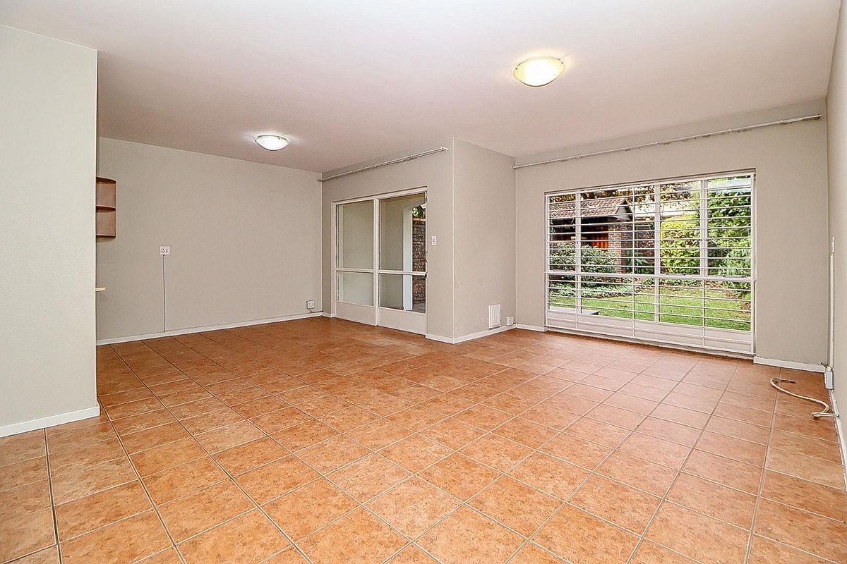 Spacious, light-filled living area featuring neutral walls, tiled flooring, and large windows with security bars, offering direct access to the garden.