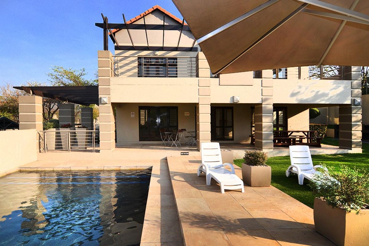 A well-maintained exterior view featuring a swimming pool, paved patio area, and a multi-level building facade with a balcony.